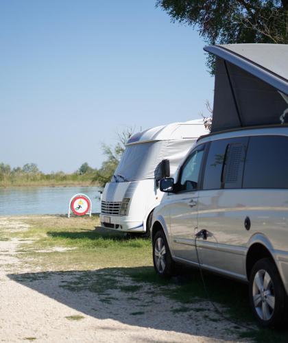 Camper parcheggiati vicino a un lago con cartello di divieto.