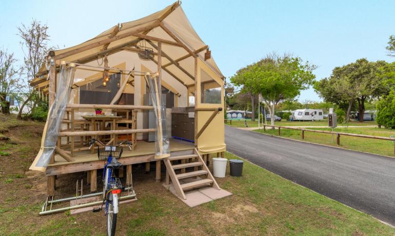 Glamping tent met veranda, omgeven door groen, nabij caravans.
