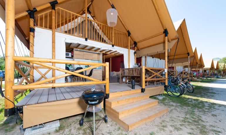 Glamping-tenten met veranda, barbecue en geparkeerde fietsen buiten.