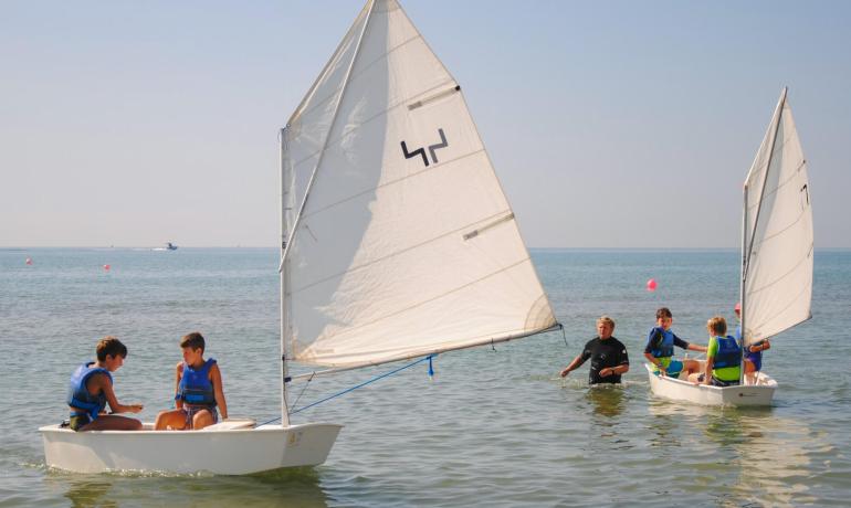 Bambini imparano a navigare su piccole barche a vela in mare.