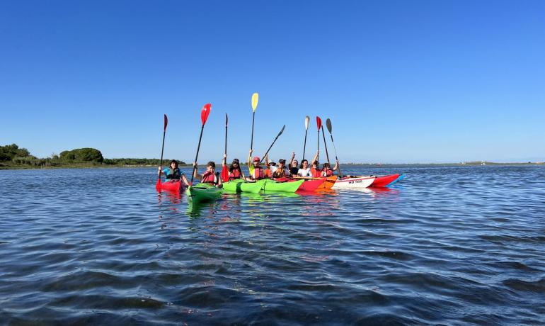 Gruppo di persone in kayak su un lago, alzano i remi al cielo.