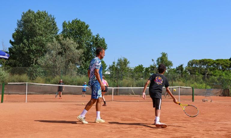 Partita di tennis su campo in terra rossa, giornata soleggiata.