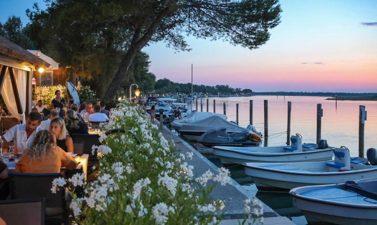 Ristorante all'aperto al tramonto, vista sul lago e barche.
